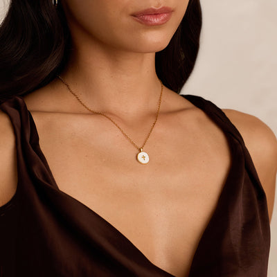 Close-up of a woman wearing a gold necklace with a pendant against a neutral background